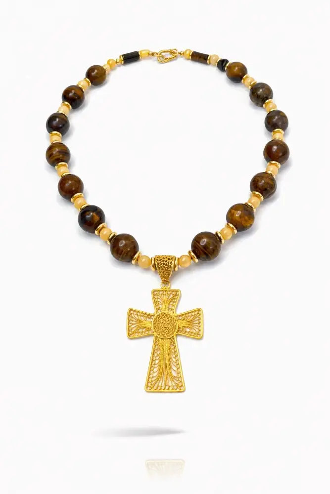Collar artesanal con grandes cuentas de ojo de tigre y detalles en oro, protagonizado por una gran cruz de filigrana dorada.
